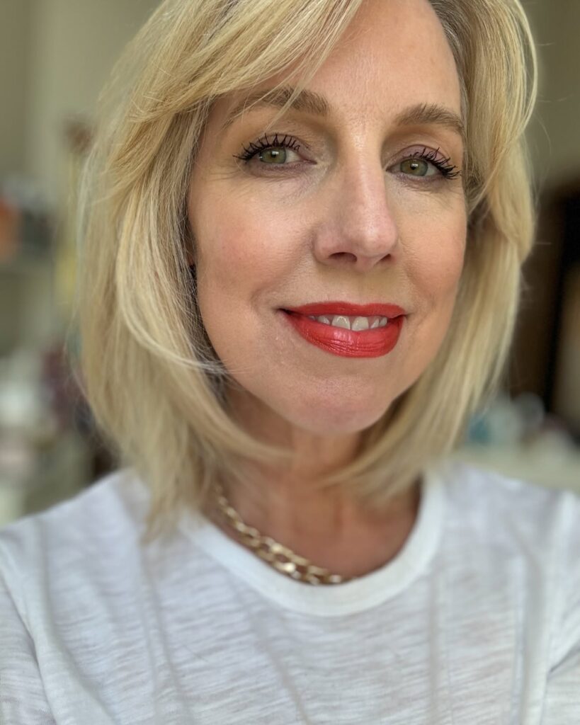 A woman smiling with a bright blonde collarbone-length bob haircut and side-swept bangs.