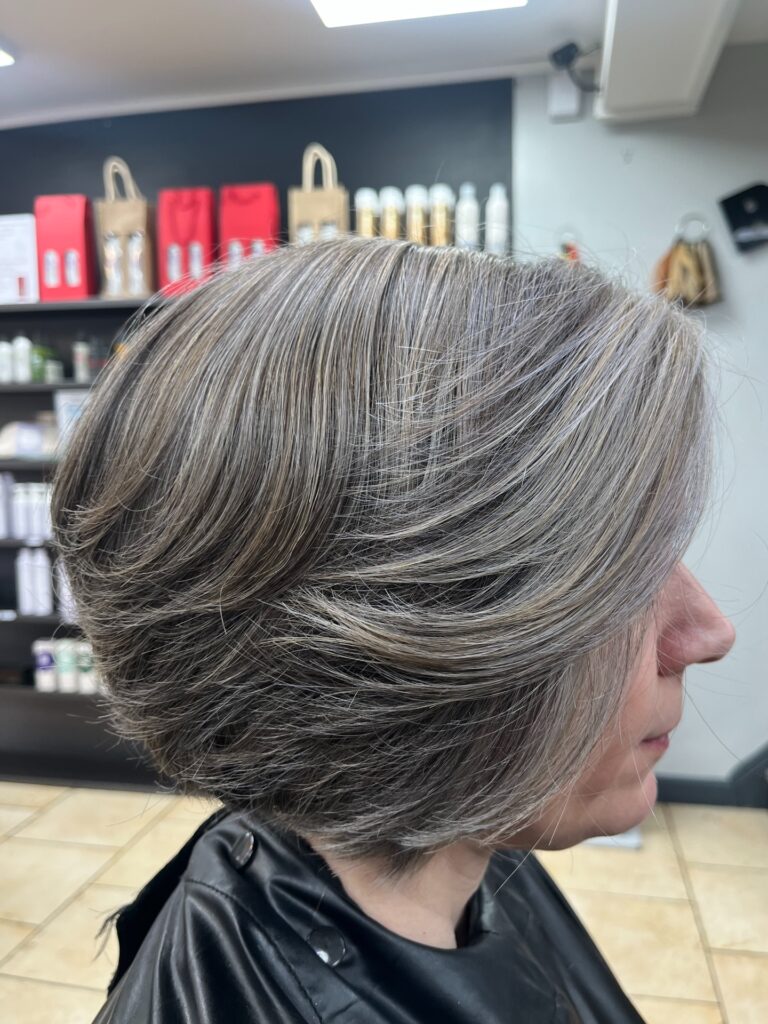 A side profile view of a woman showing a layered, stacked bob haircut with salt-and-pepper silver highlights.