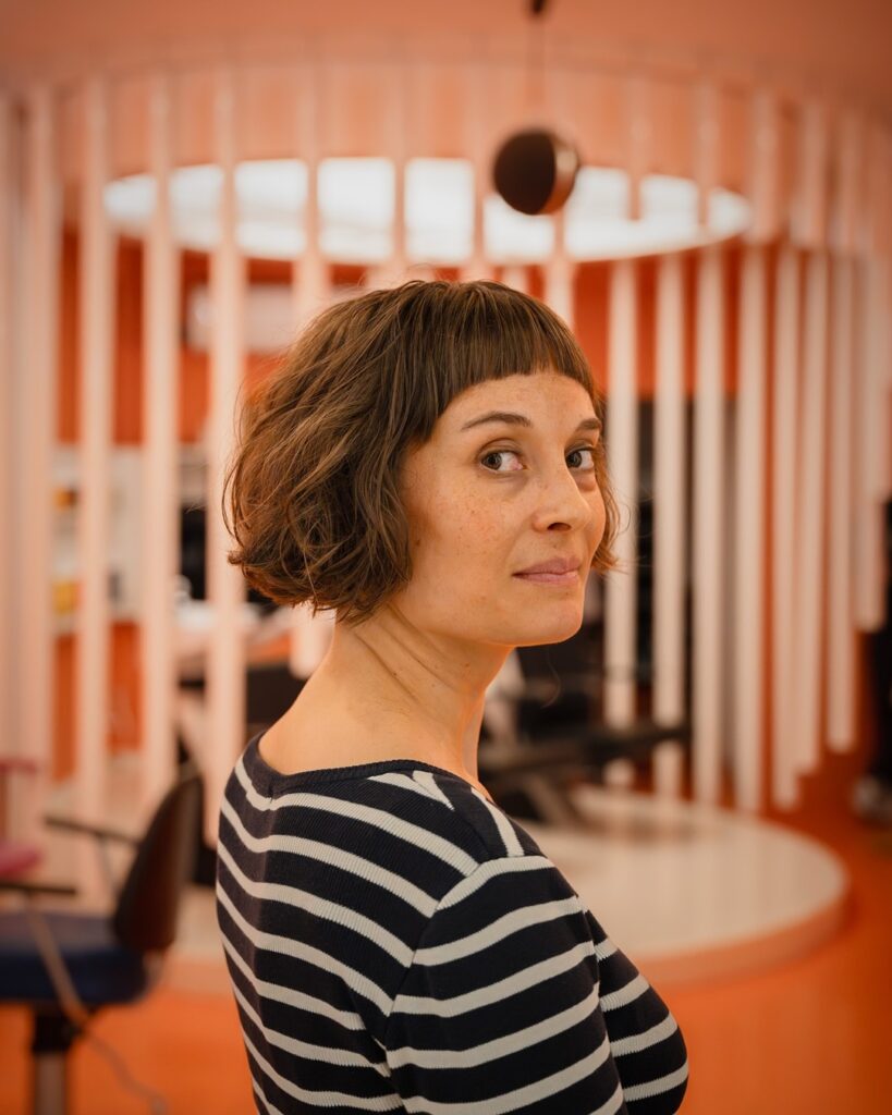 A woman looking over her shoulder showcasing a chin-length wavy brunette bob haircut with straight micro bangs.