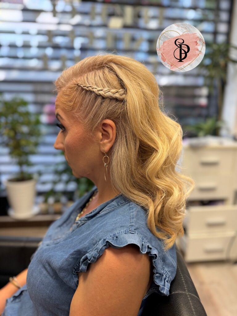 A side profile view of a woman over 60 showcasing a shoulder-length honey-blonde hairstyle with soft waves and a small accent braid pinned to the side.