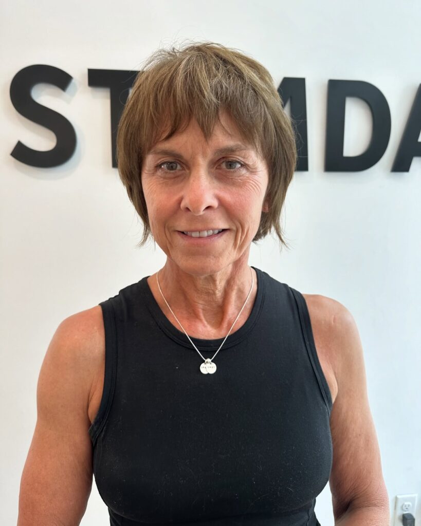 A front view of a smiling woman over 60 with a textured chin-length brown shag haircut and wispy bangs.