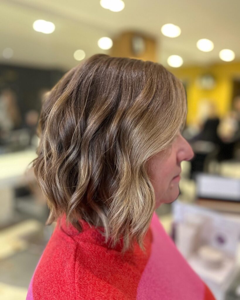 A woman showing a side profile of a neck length golden brunette lob with soft waves.