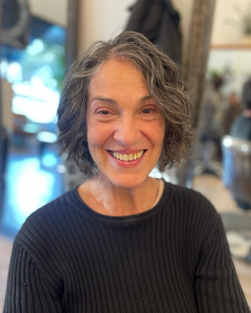 A smiling woman with a chin length salt and pepper wavy bob.