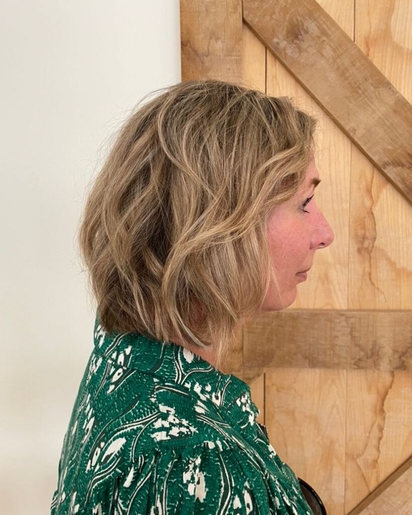 A woman showing a side profile of a neck length sandy blonde wavy lob with golden highlights.