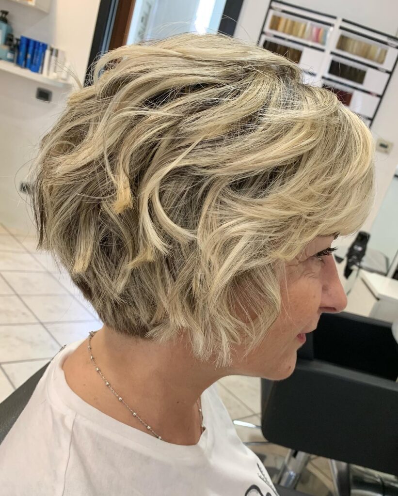 A woman showing a side profile of a champagne blonde bixie cut with piecey waves and textured layers.