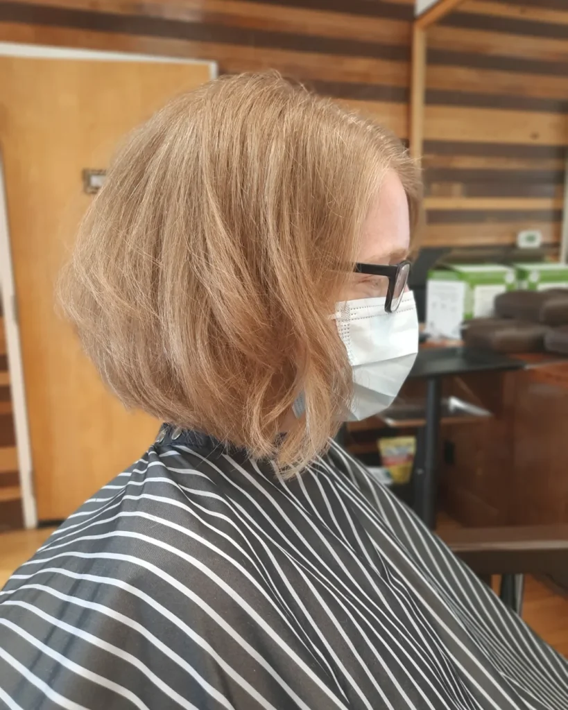A woman showing a side profile of a chin length honey blonde bob with soft waves.