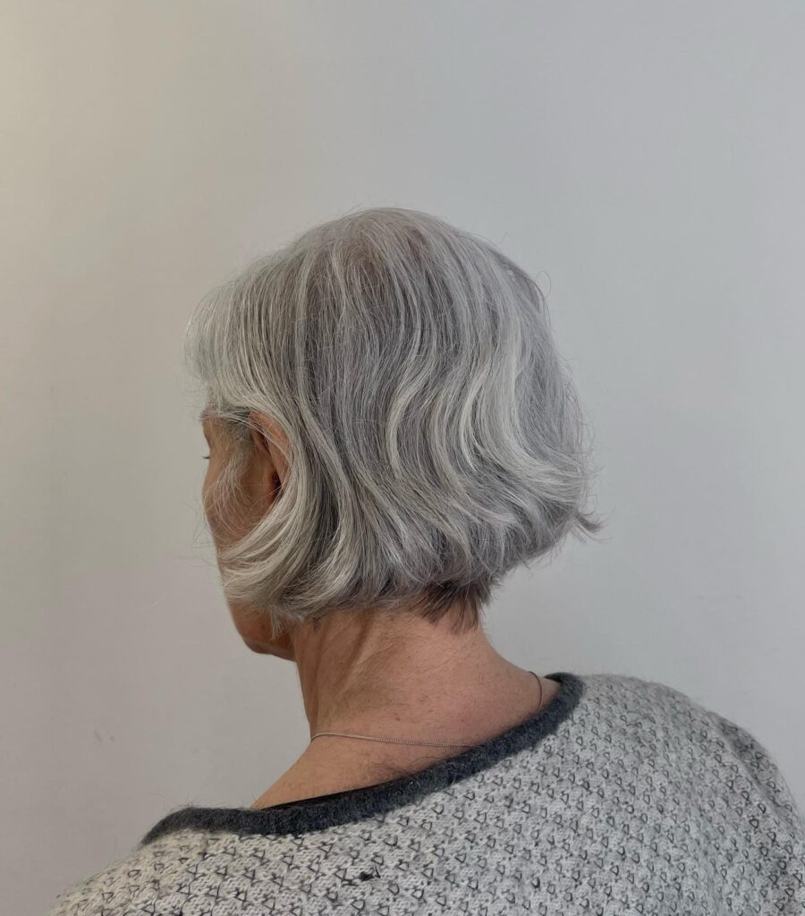 A woman showing the back profile of a chin length silver wavy French bob.