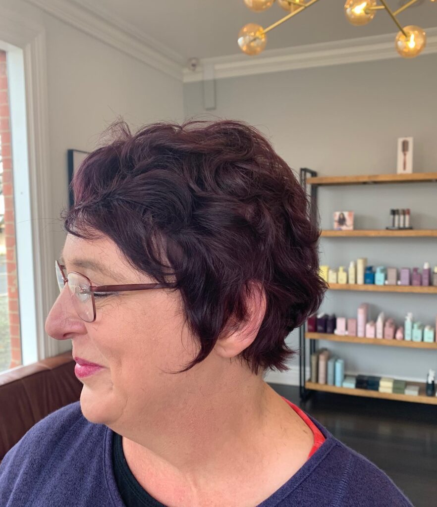 A woman with a short wavy deep plum pixie cut featuring tapered layers and voluminous texture.