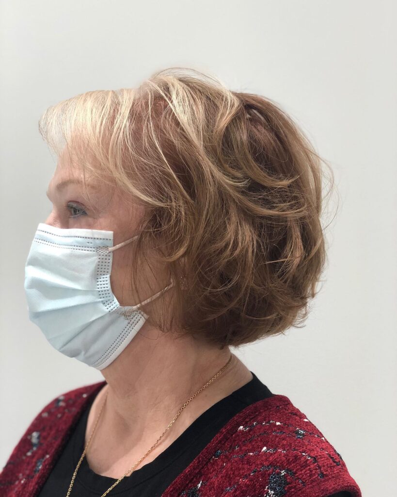 A side profile of a woman with a layered honey blonde bob haircut featuring golden highlights and voluminous texture.