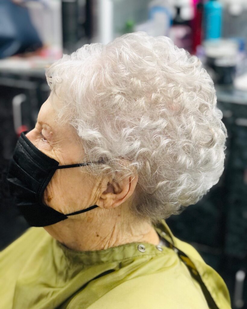 A woman with a short curly silver pixie haircut viewed from the side profile.