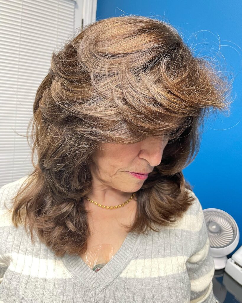 A woman with a voluminous chestnut brown shag haircut featuring feathery crown layers and thick sweeping bangs.