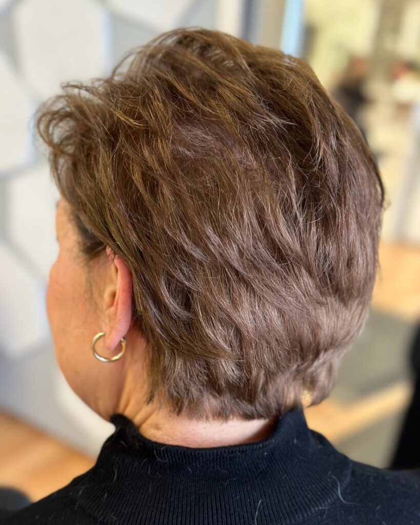 A view from behind of a woman with a textured chocolate brown pixie haircut featuring piecey volume and natural waves.