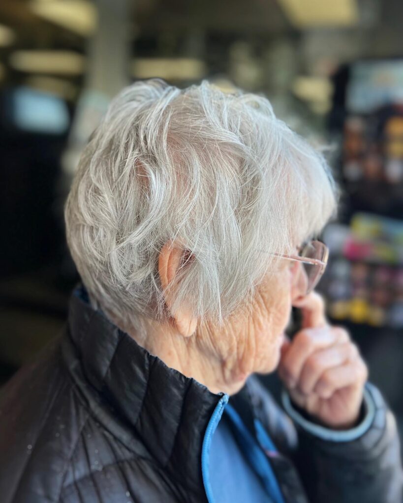 A side profile view of a woman with an ultra-short natural silver pixie haircut featuring spiky texture on top and a dark tapered undercut.