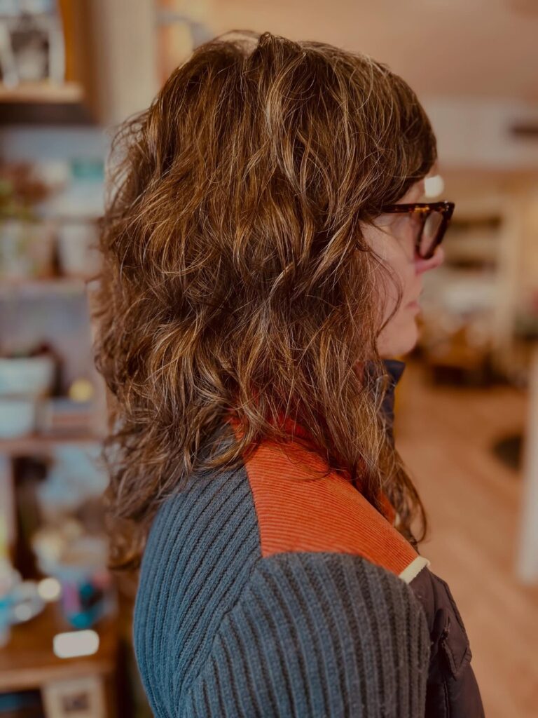 A side profile view of a woman with medium-length curly brunette hair featuring warm caramel highlights and textured layers.