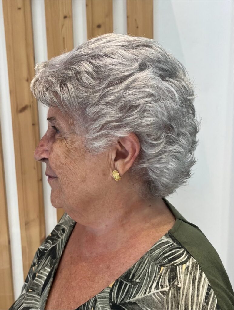 A side profile view of an older woman with a short sculpted silver shag haircut showcasing natural waves and piecey crown layers.