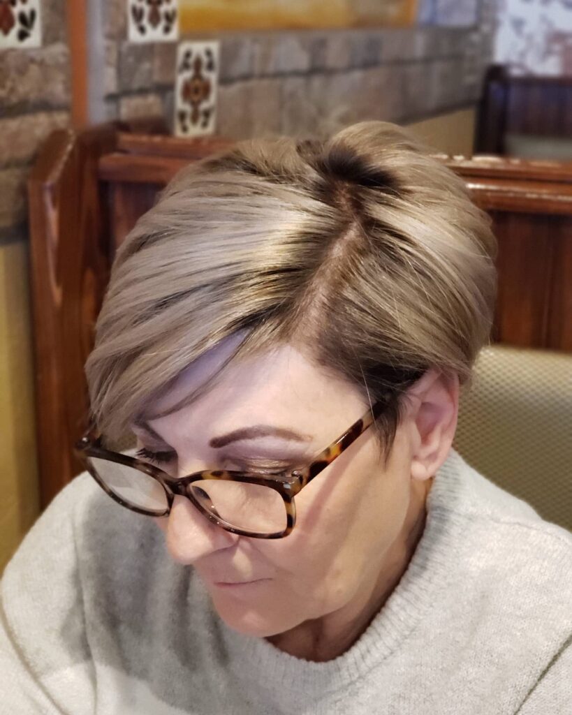 A top-down view of a woman with a voluminous dark blonde asymmetrical pixie haircut featuring a deep side part.