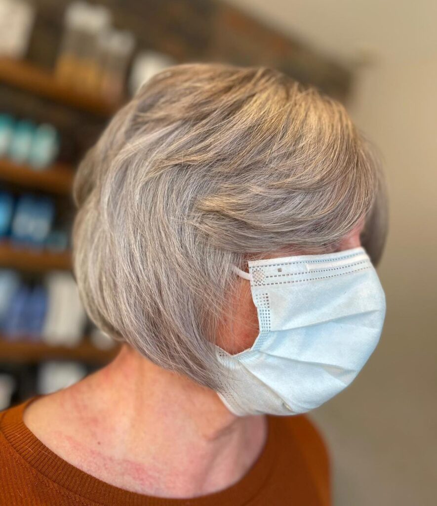 A woman with a chin-length ash grey bob featuring feathered layers and side-swept bangs.