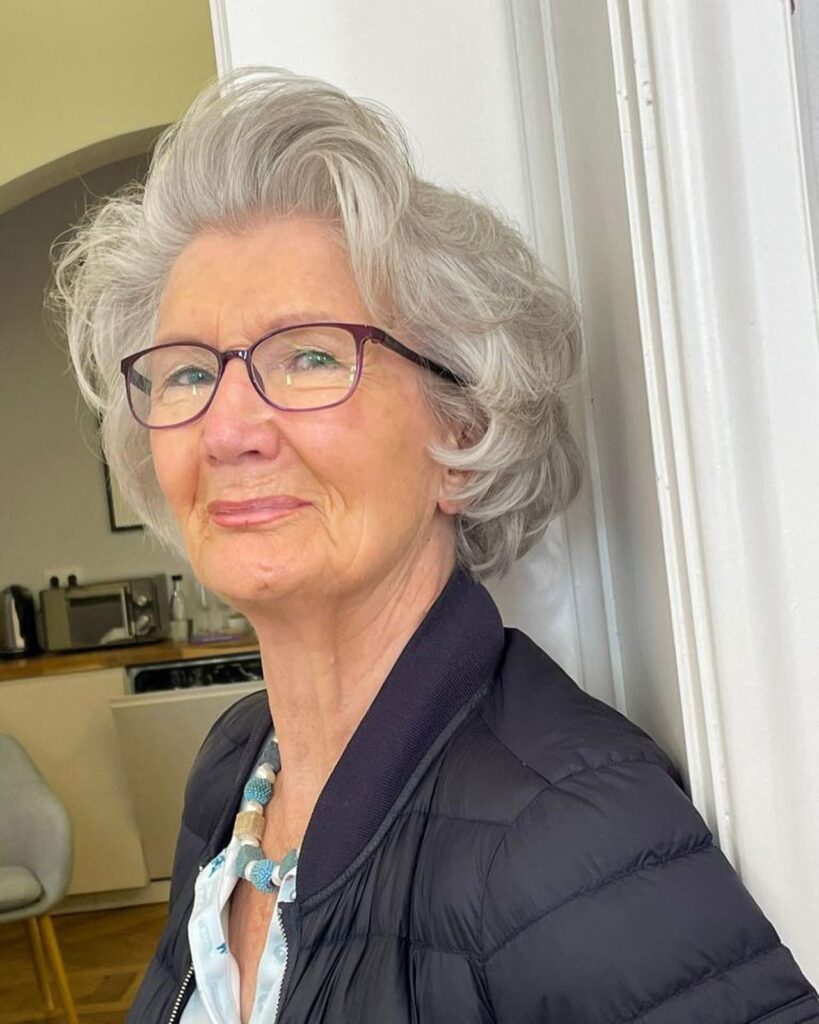 A smiling woman over 60 with a voluminous silver pixie haircut styled with soft swept-back curls.
