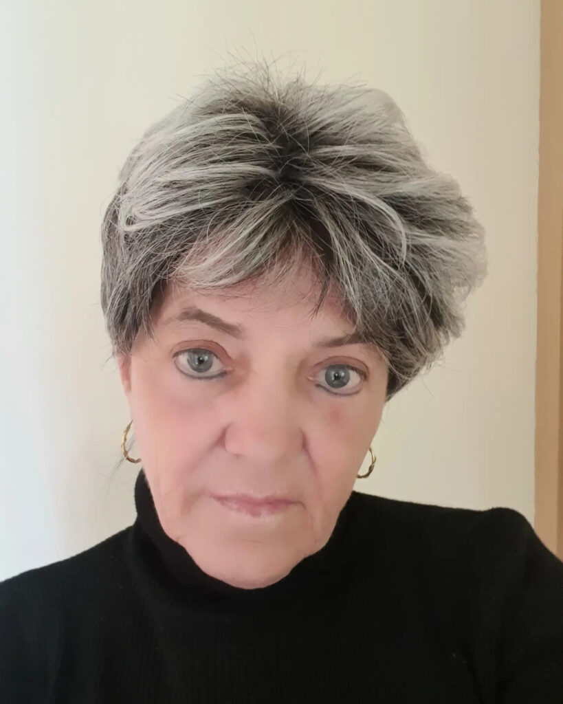 A woman with a textured salt-and-pepper pixie haircut featuring spiky layers on top and a feathered fringe.