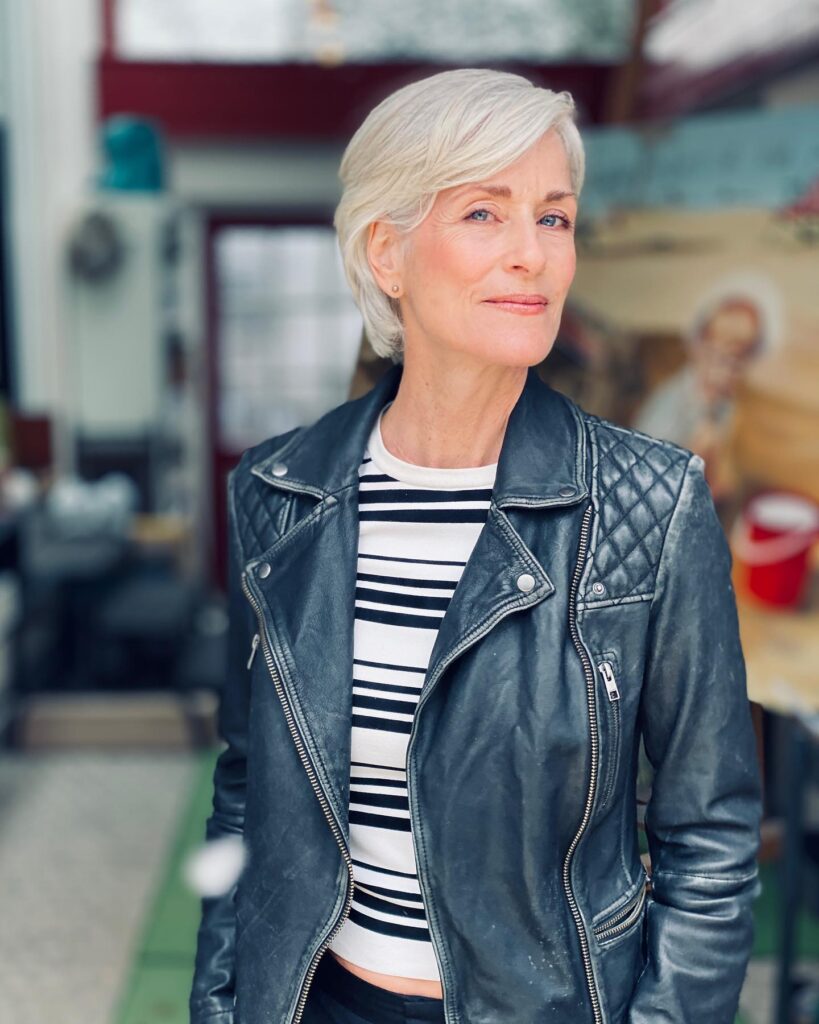 A woman wearing a black leather jacket poses with a sleek, side-swept, icy white short bob.