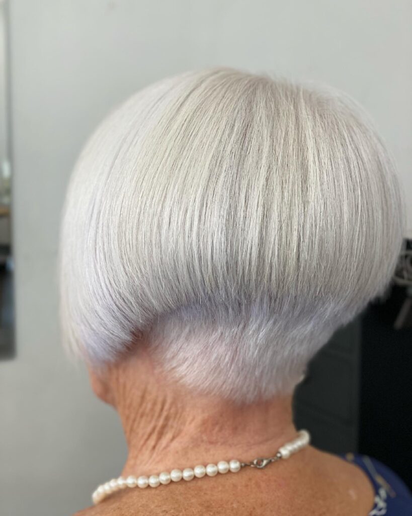 A back view of a woman with a sleek, platinum white inverted bob featuring a neatly tapered nape and smooth, rounded layers.
