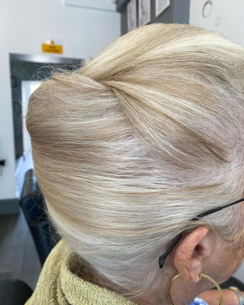 A back view of a woman with creamy blonde hair styled in a smooth and elegant French twist updo.
