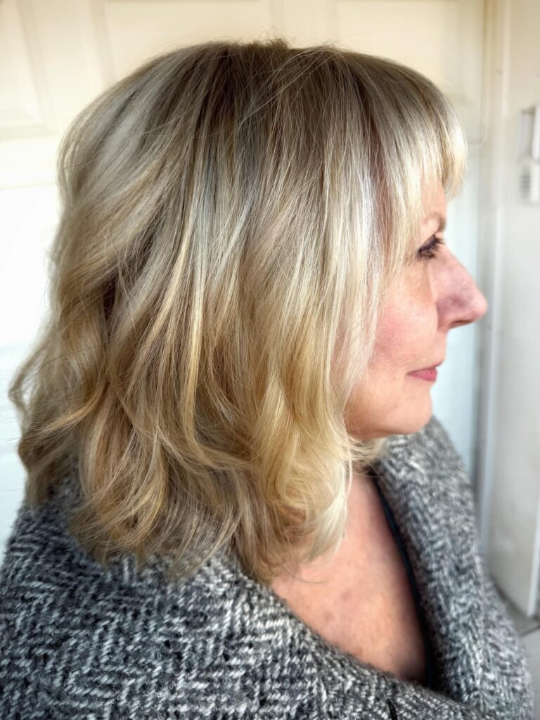 A woman with a shoulder-length champagne blonde lob featuring textured waves and soft, wispy bangs.