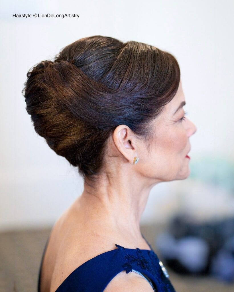 A side profile of a woman with deep brown hair styled in a sleek and elegant French twist with overlapping smooth sections.