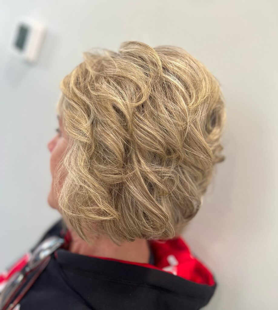 A side profile of a woman with a chin-length blonde bob styled in loose, voluminous tousled curls.