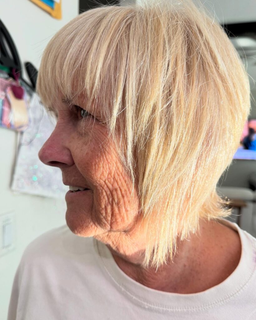Layered blonde bob with wispy bangs and feathered textured ends.