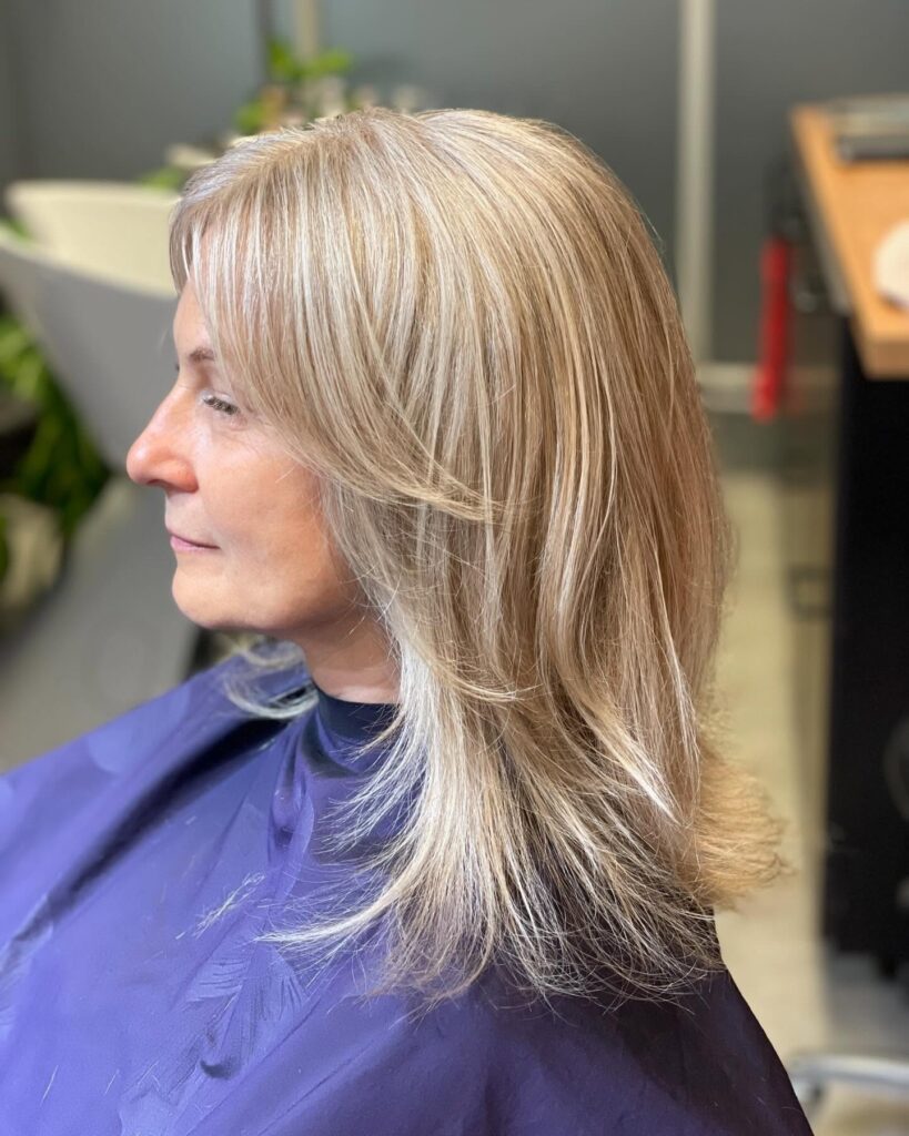 A woman viewed from the side profile showing off her medium-length layered straight sandy blonde hair with bright platinum highlights.