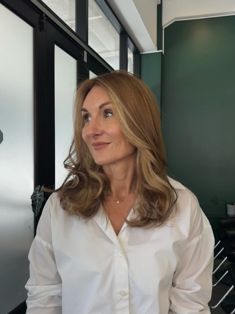 A side view of a woman with a straight shoulder length brunette haircut featuring golden blonde balayage highlights.