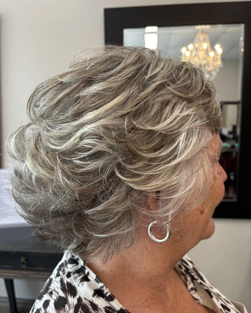 A back and side view of a woman in a salon showing off a layered shoulder length dark brunette haircut with warm golden highlights.