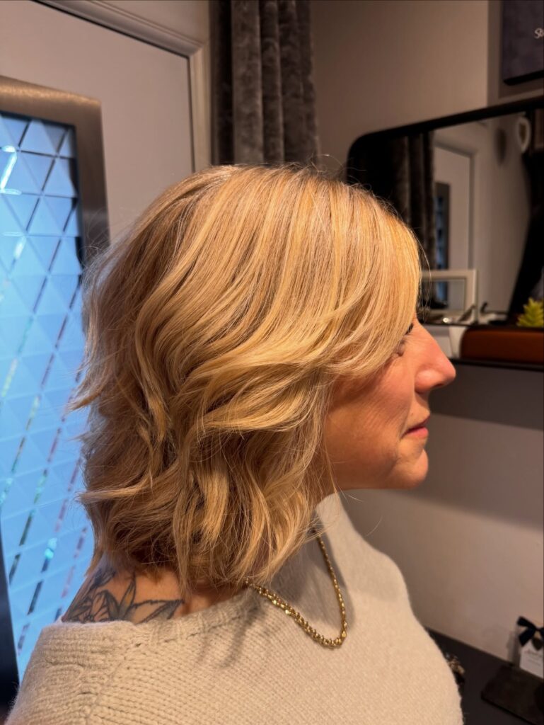 A side profile of a woman showing off a textured shoulder-length golden blonde shag haircut with soft tousled waves.
