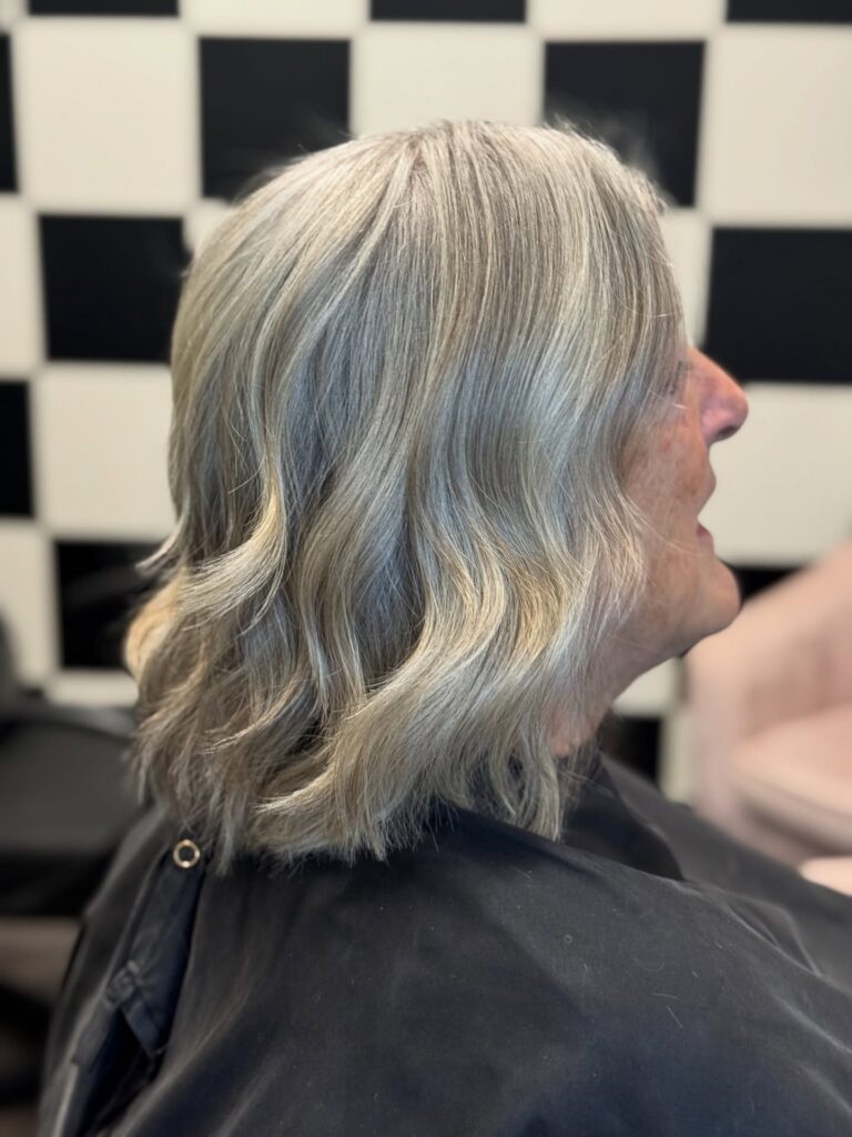 A side profile view of a woman showcasing her shoulder-length wavy gray hair with platinum highlights and textured ends.