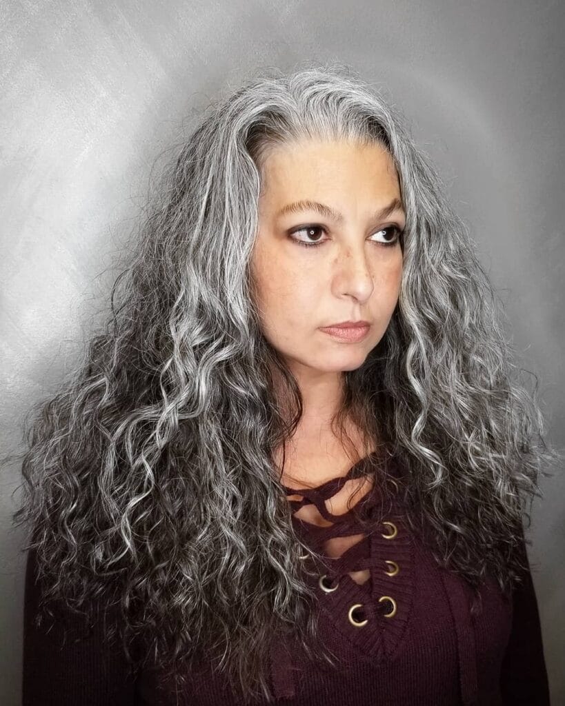 Long salt and pepper curly hairstyle with loose flowing curls past the shoulders.