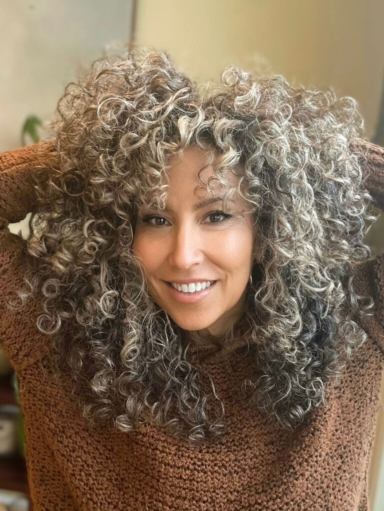Shoulder length salt and pepper curly hairstyle with layered volume and soft texture.