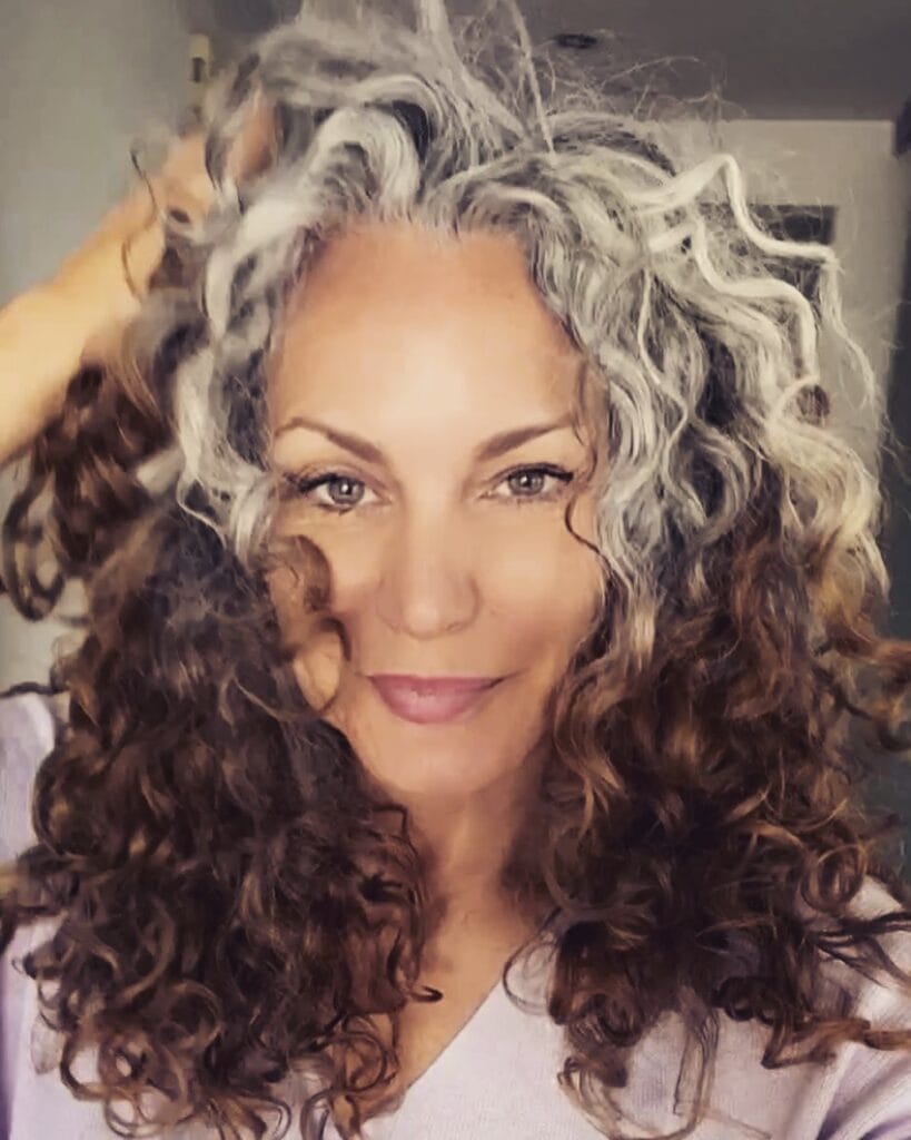 Long layered curls with silver roots and dark brown curly lengths.