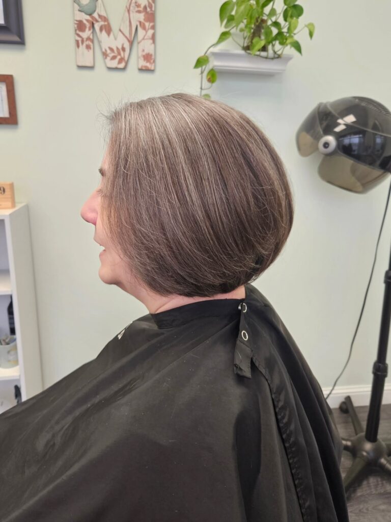 An older woman smiles warmly while displaying a textured silver pixie cut with spiky crown layers and natural gray lowlights.