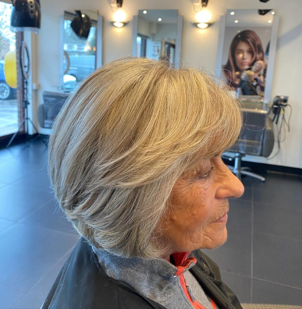 An older woman from a side profile view displays a elegant chin-length sandy blonde bob with sweeping feathered layers.