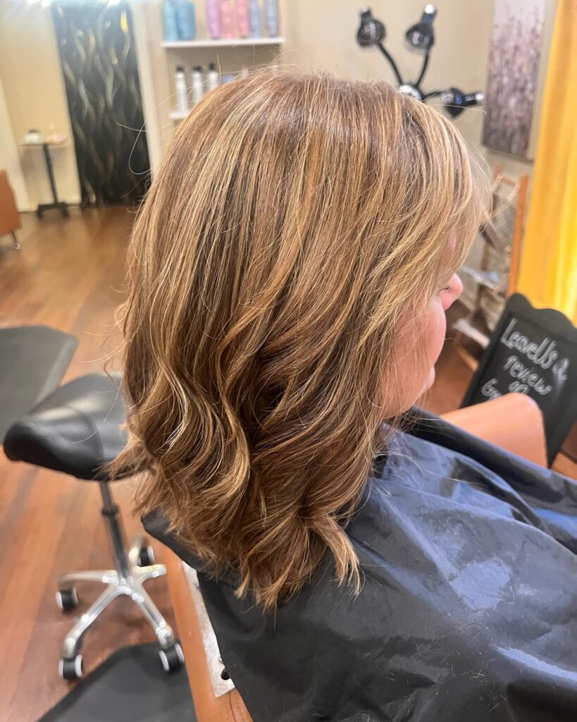 A woman from a side profile view displays a rounded jaw-length honey blonde bob haircut with fine crown layers and pale blonde highlights.