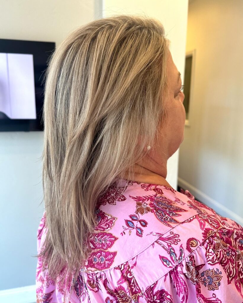 A woman from a side profile perspective showcasing straight, shoulder length ash blonde hair with subtle long layers.