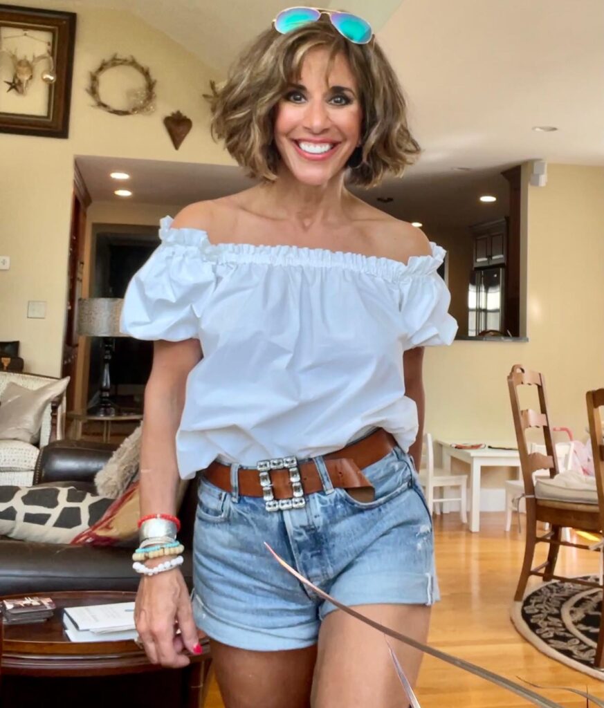 A smiling woman over 60 with a voluminous, layered brunette bob haircut with honey highlights and soft bangs.