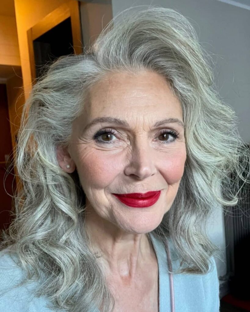A woman over 60 with medium-length silver hair styled in voluminous cascading waves with a deep side part.