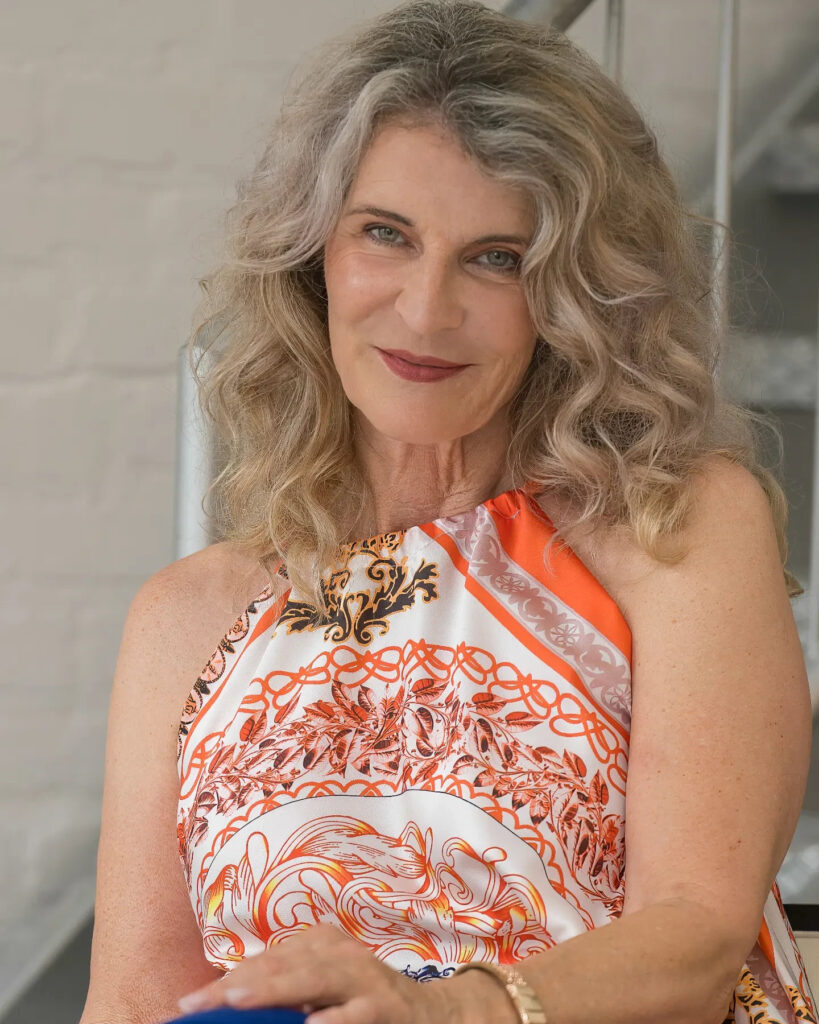 An elegant woman over 60 with shoulder-length voluminous curly blonde and gray hair worn in loose cascading waves.