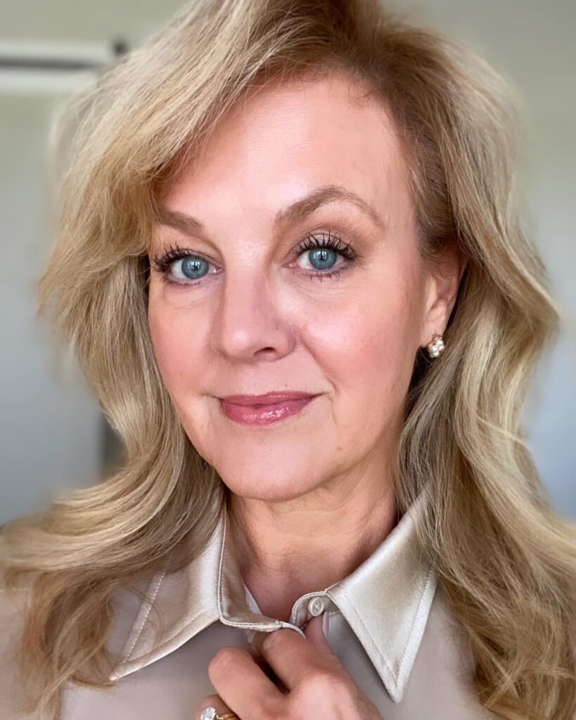 A beautiful woman over 60 with medium-length strawberry blonde hair styled in soft, elegant waves with a voluminous side sweep.