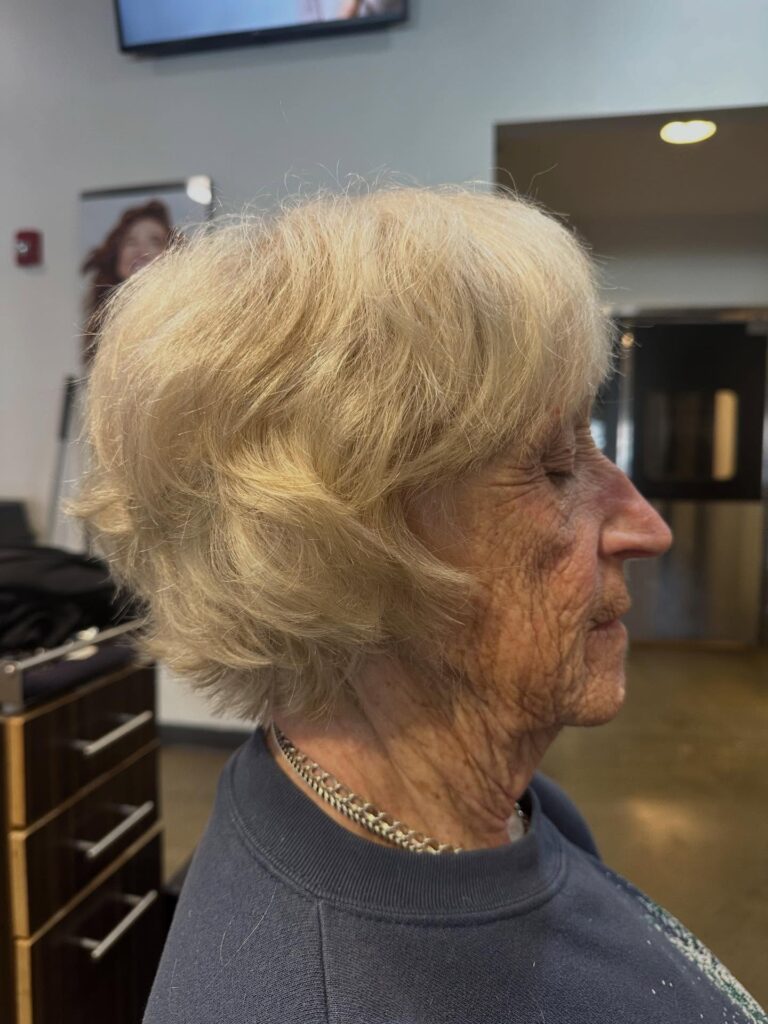 A woman over 60 shown in profile with a short feathered honey blonde haircut featuring full wispy bangs.
