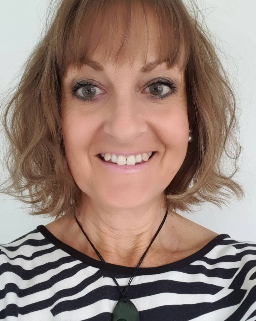 A smiling woman over 60 with a neck-length wavy light brown bob and wispy bangs.
