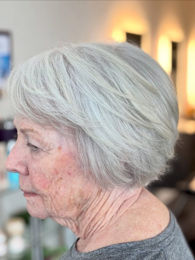 A side profile of an older woman with an icy white feathered bixie haircut showing soft piecey layers.