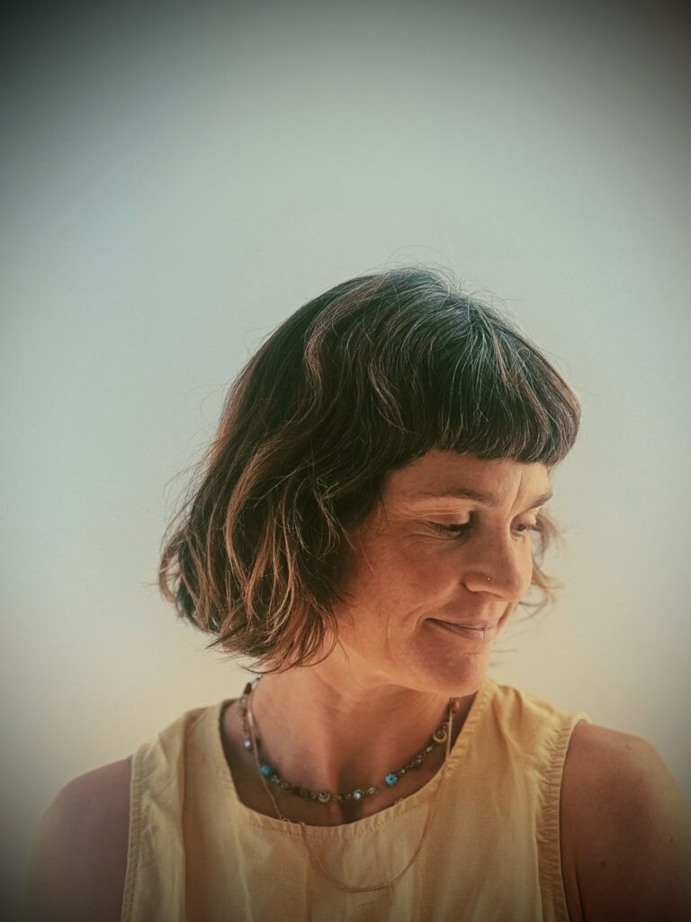 A woman with a chin-length wavy brunette French bob with blunt bangs and blonde tips looking down.